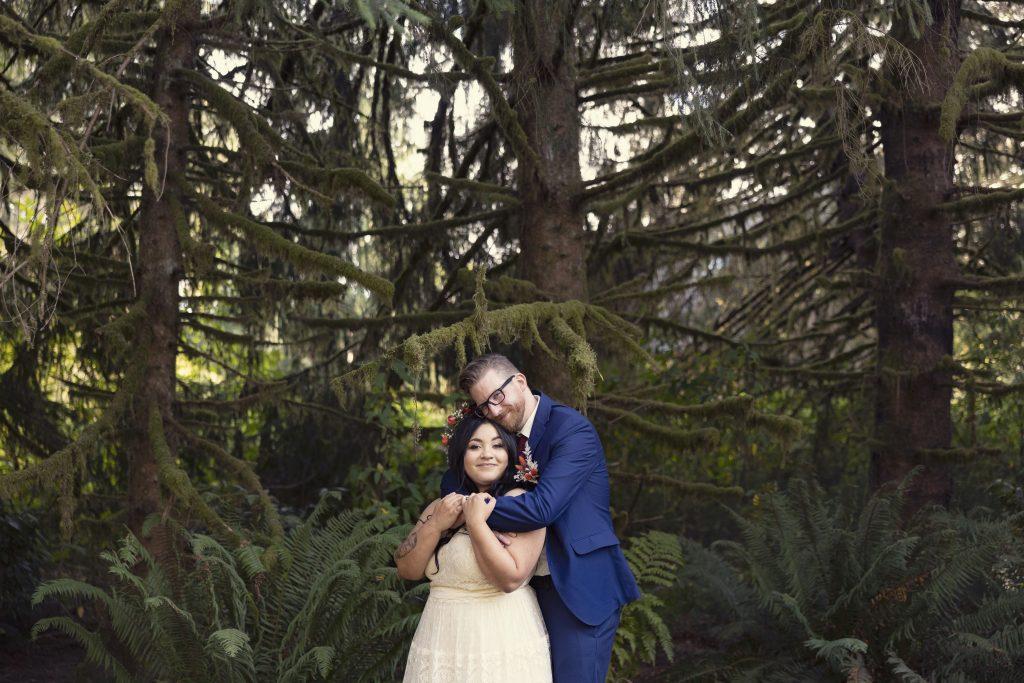 Bride groom couple standing in the forest, trees, waterfront wedding venue River Valley Oasis Snohomish