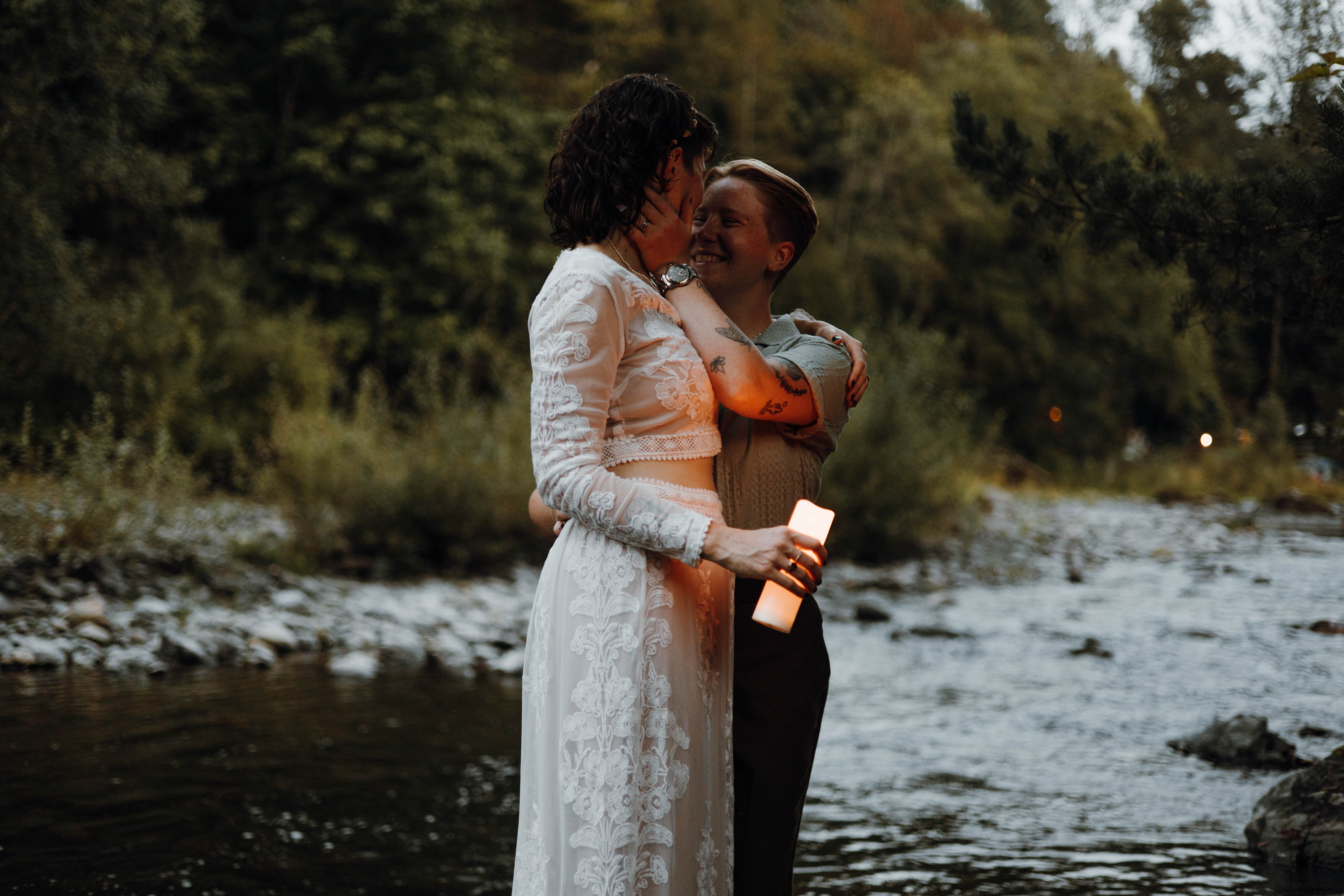 Bride and groom lit by lanterns along the riverbank after dark
