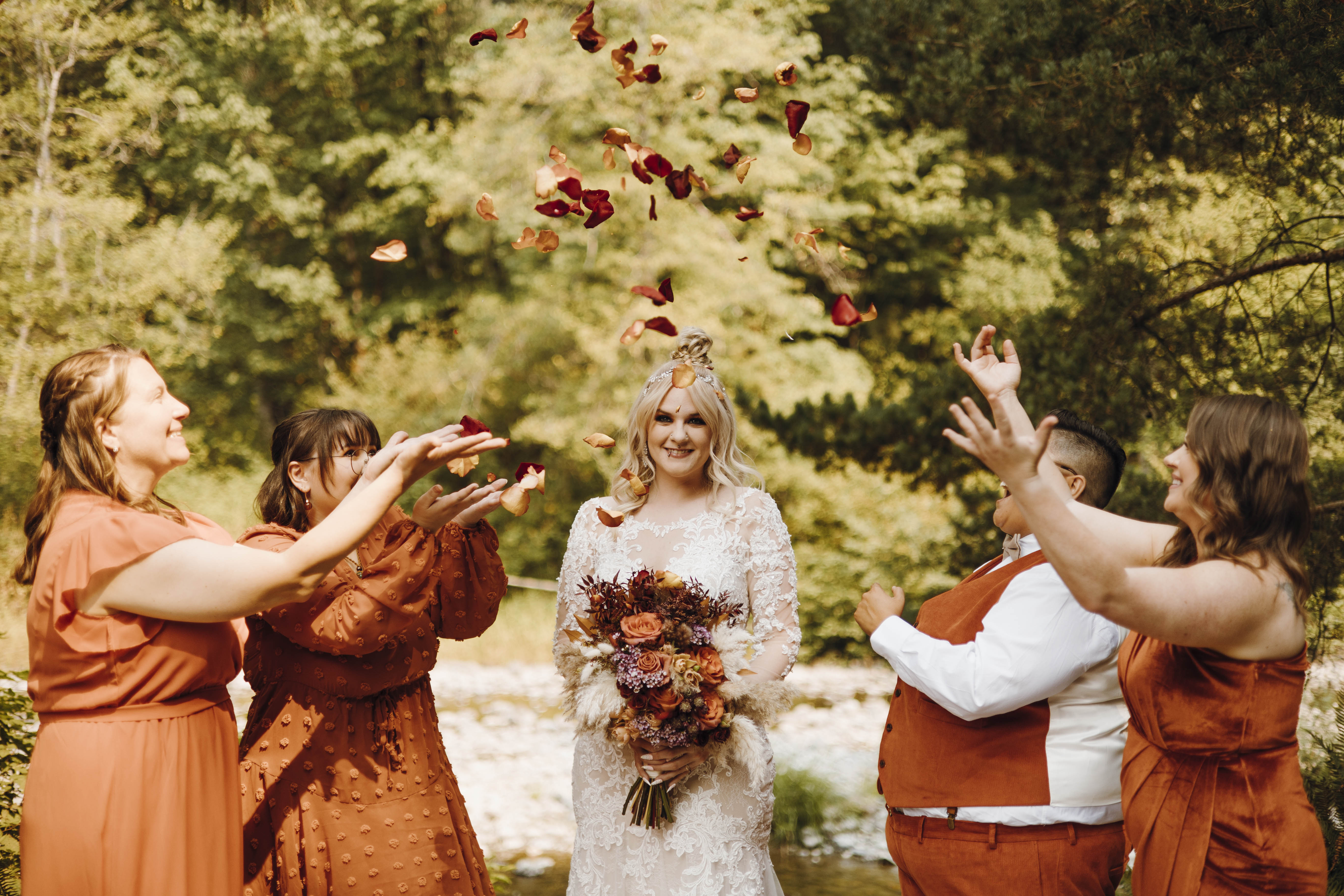 bride with bridesmaids throwing rose petals with river in background