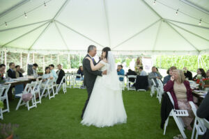 Guests seated at wood tables during the reception dinner as bride dances with father