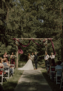 couple stands under an arch with red linens